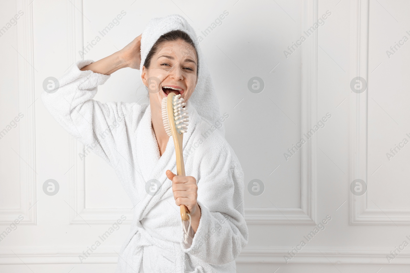 Photo of Spa day. Beautiful woman with face mask and brush singing indoors, space for text