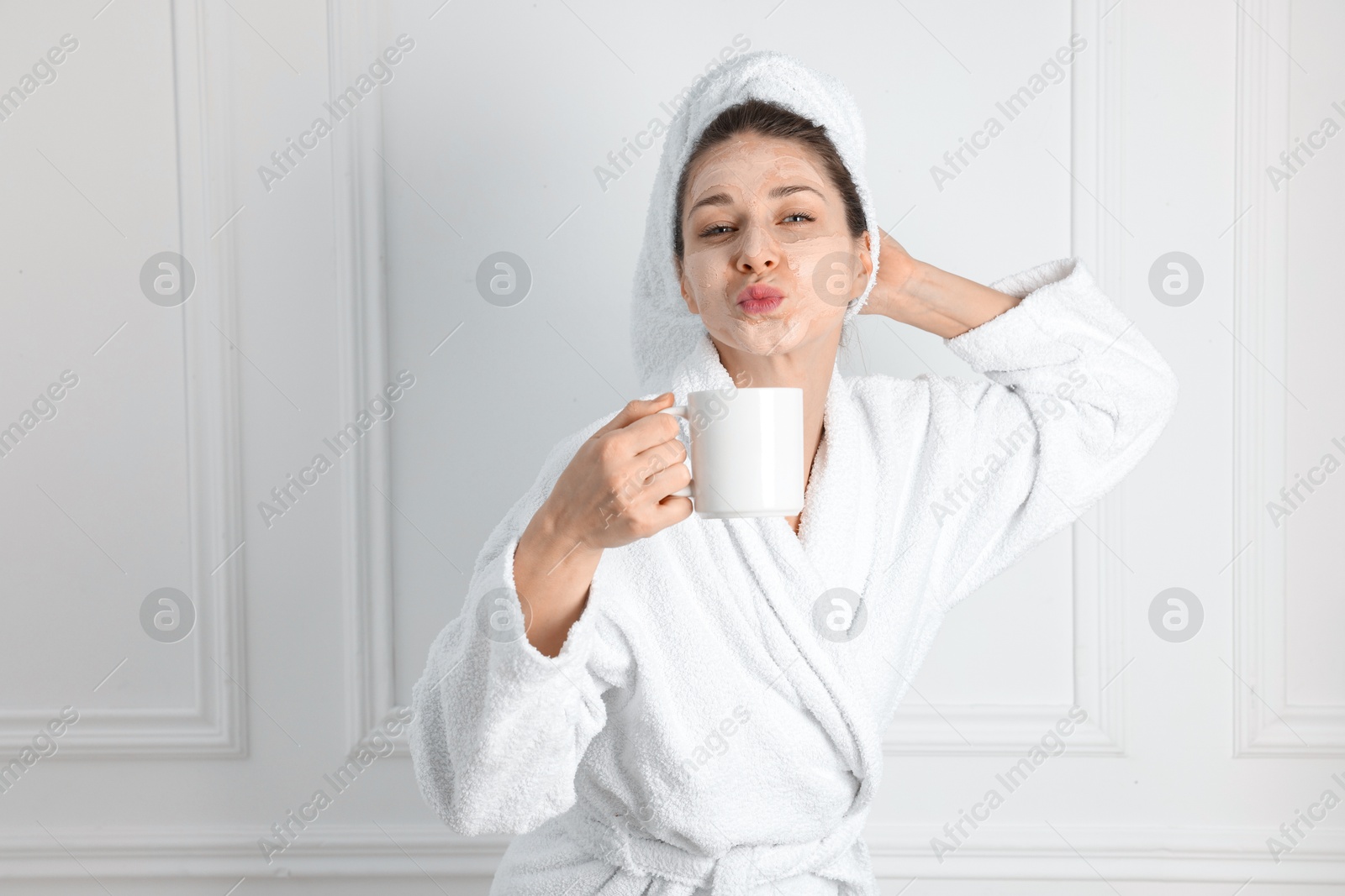 Photo of Spa day. Beautiful woman with face mask and cup of drink indoors, space for text