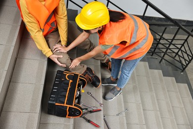 Photo of Accident at work. Woman helping her injured colleague on stairs indoors, closeup