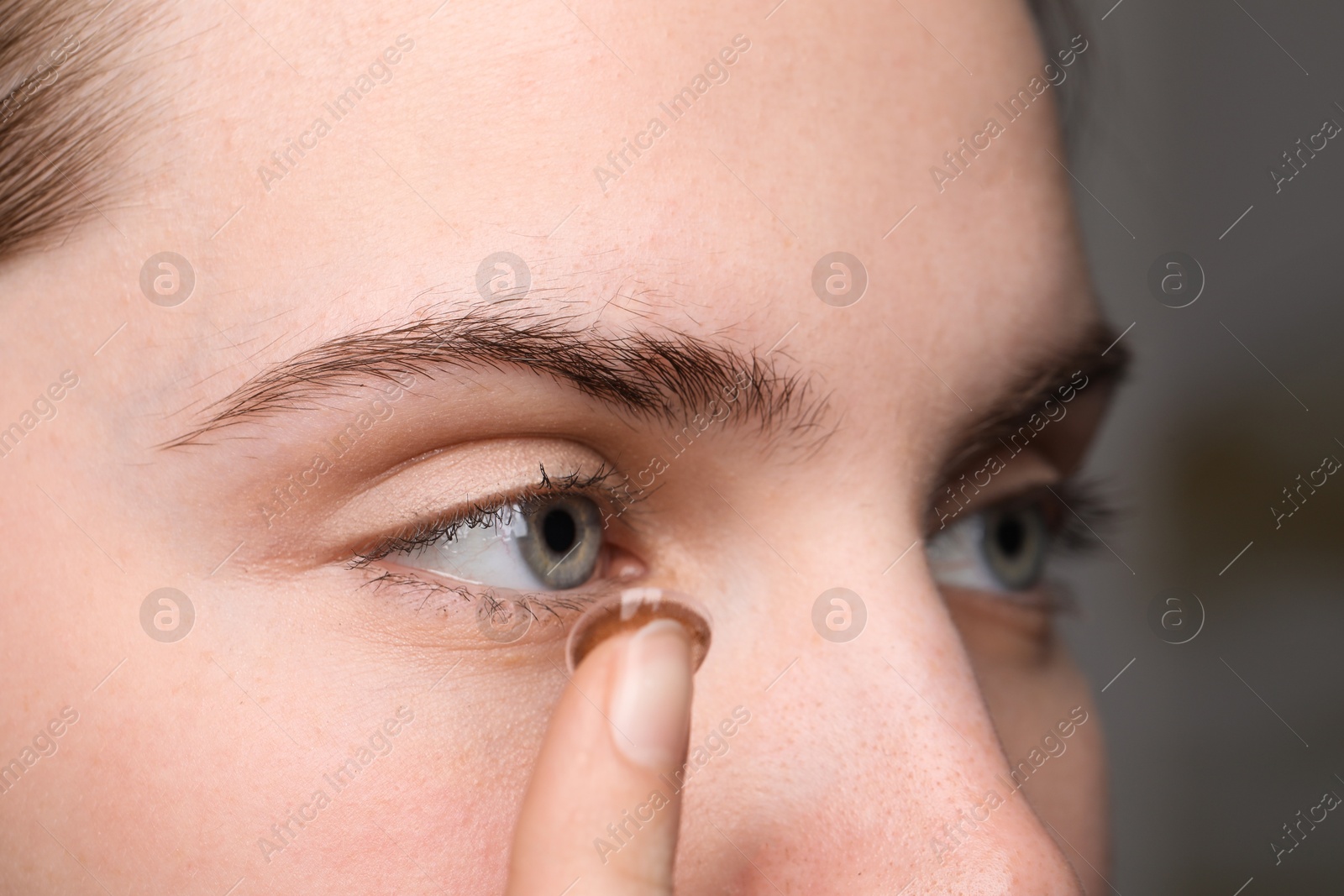 Photo of Young woman putting in color contact lens on blurred background, closeup