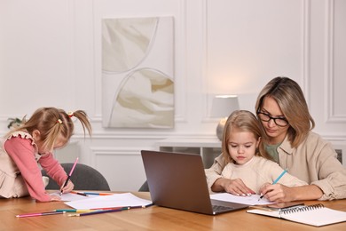 Photo of Work-family balance. Single mother with her children drawing at wooden table indoors