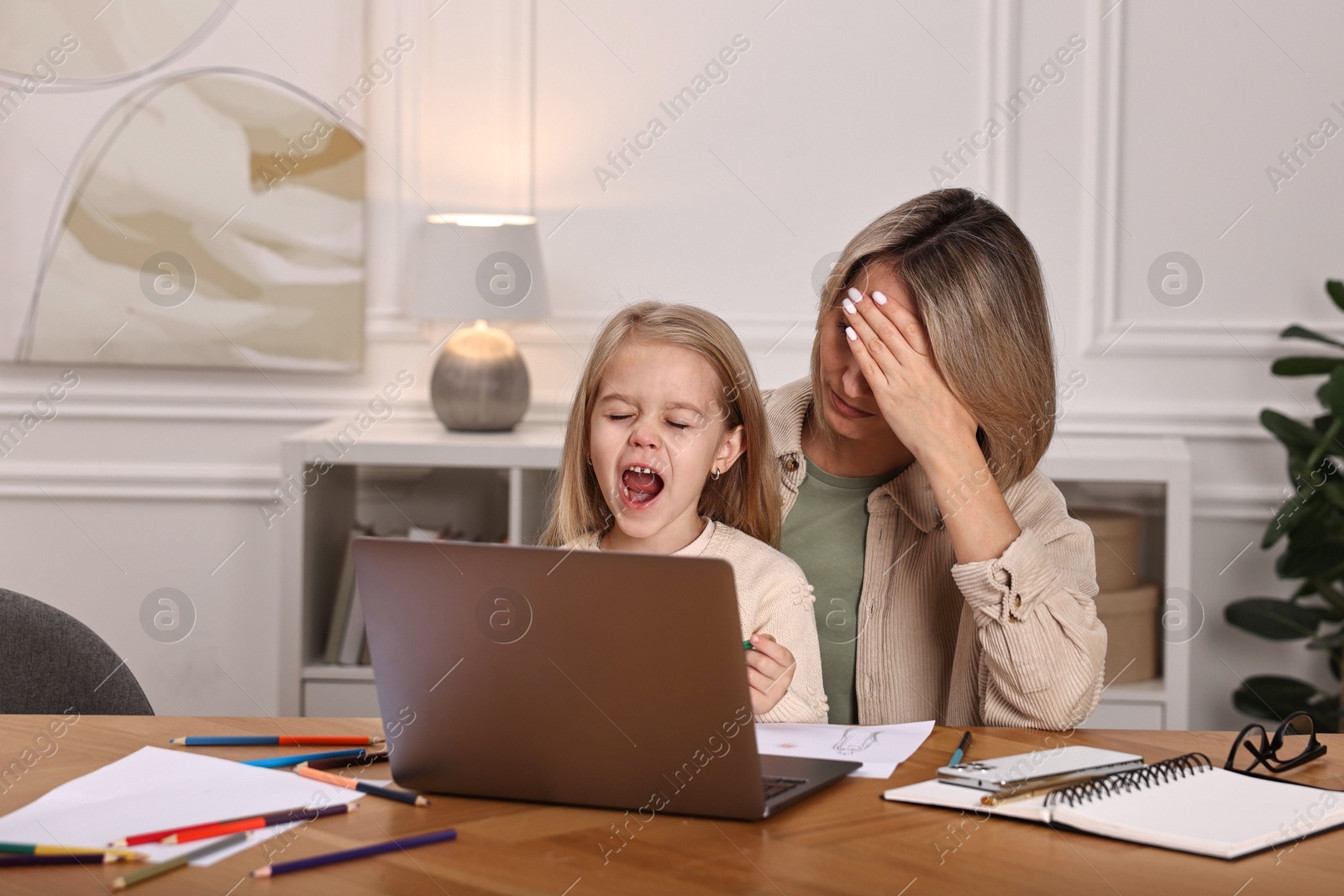 Photo of Work-family balance. Single mother and her naughty screaming daughter at wooden table indoors