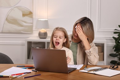 Photo of Work-family balance. Single mother and her naughty screaming daughter at wooden table indoors