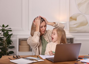 Photo of Work-family balance. Single mother and her naughty screaming daughter at wooden table indoors