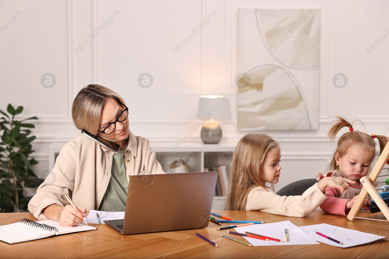 Photo of Work-family balance. Single mother talking by smartphone and her children at wooden table indoors