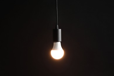 Photo of Glowing light bulb hanging on dark background