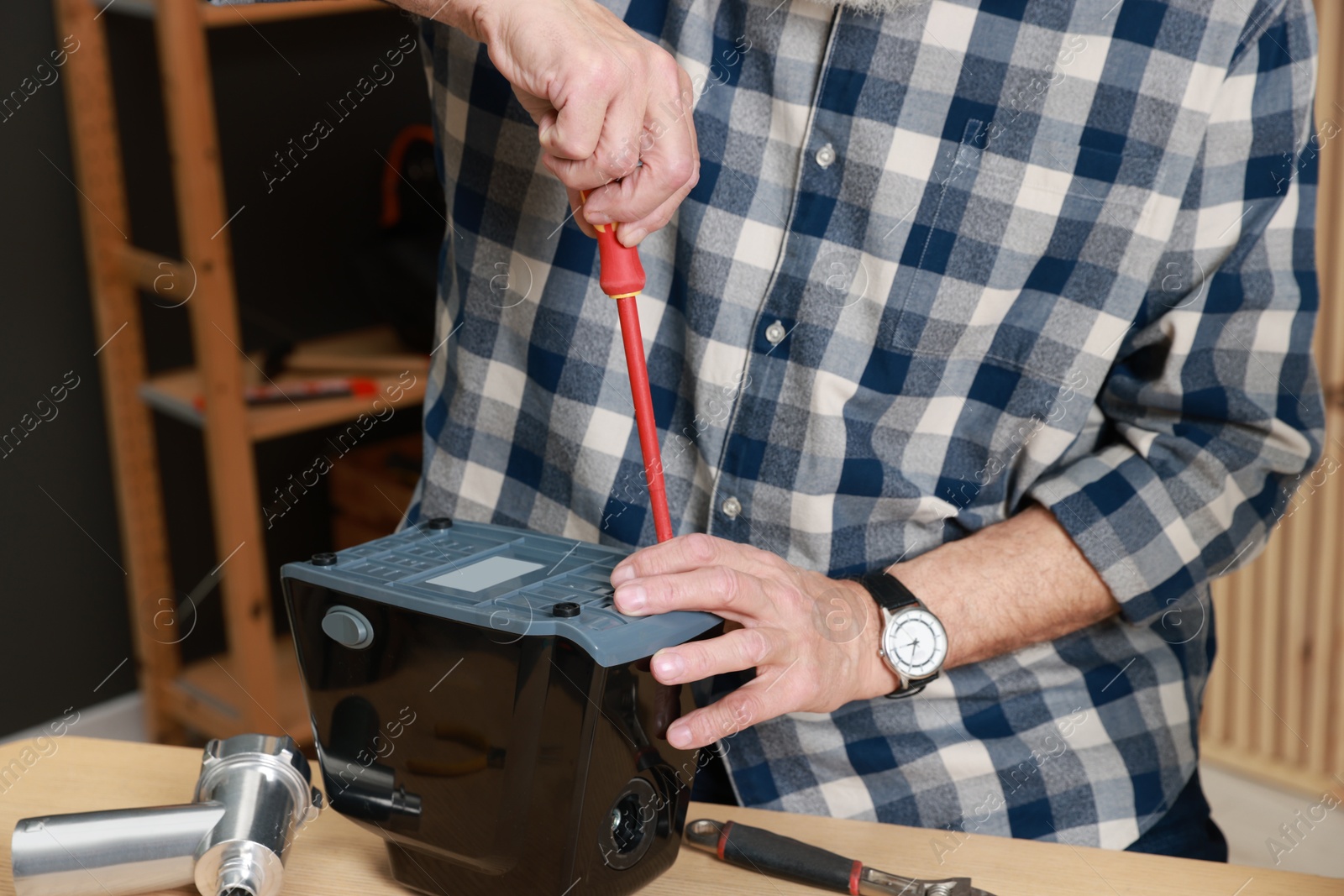 Photo of Relaxing hobby. Senior man repairing meat grinder with screwdriver in workshop, closeup