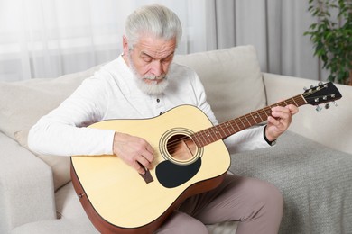 Photo of Relaxing hobby. Senior man playing guitar on sofa at home