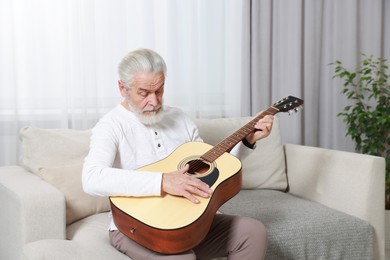 Photo of Relaxing hobby. Senior man playing guitar on sofa at home