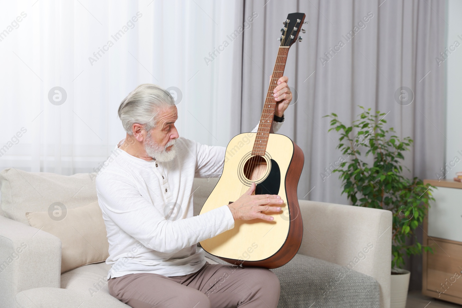 Photo of Relaxing hobby. Senior man playing guitar on sofa at home