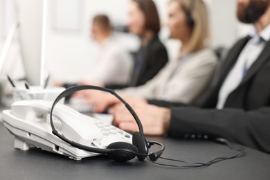 Photo of Technical support call center. Team of operators working at table in office, focus on phone and headset