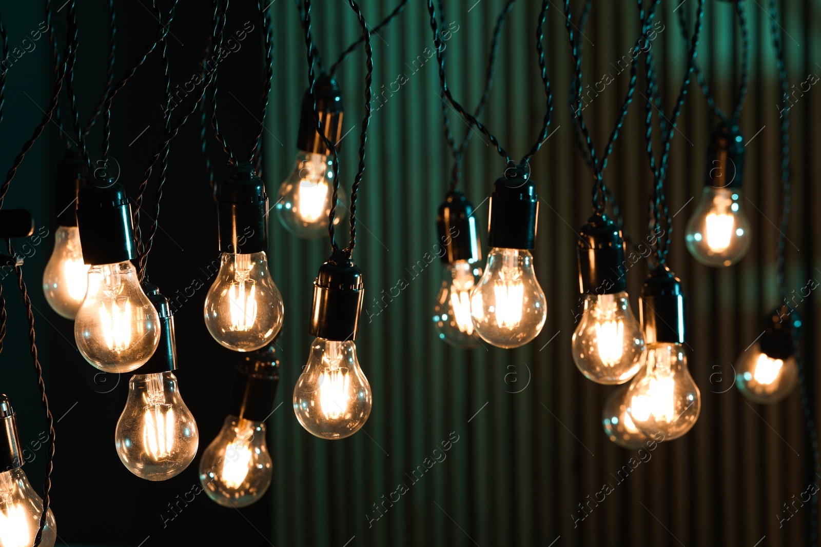 Photo of Glowing light bulbs hanging on color background, closeup