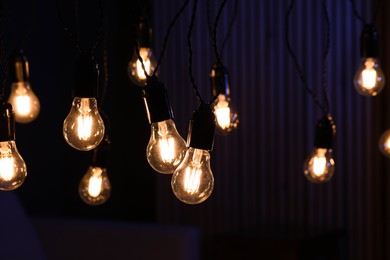 Photo of Glowing light bulbs hanging indoors, closeup view