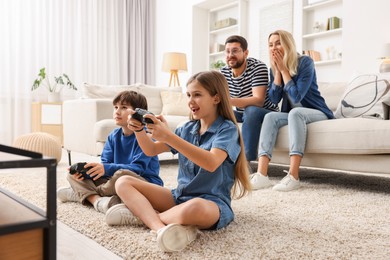 Cute kids playing video games while their parents resting on sofa indoors