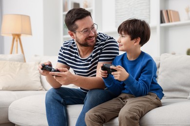 Photo of Father and his son playing video games on sofa in living room