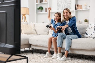 Photo of Happy mother and her daughter playing video games on sofa in living room