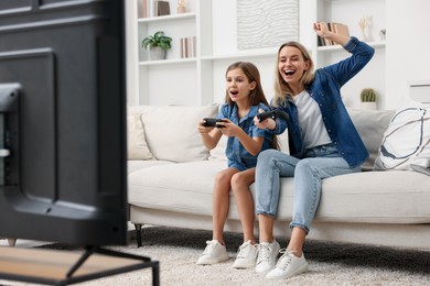 Photo of Happy mother and her daughter playing video games on sofa in living room