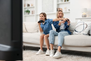 Photo of Happy mother and her daughter playing video games on sofa in living room