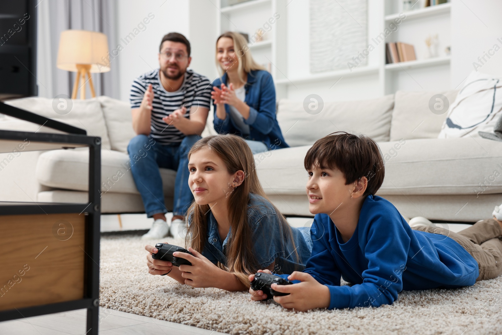 Photo of Cute kids playing video games while their parents resting on sofa at home, selective focus