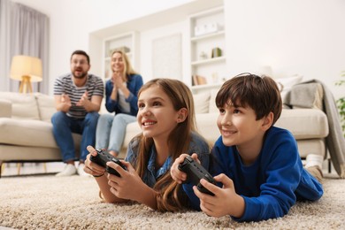 Photo of Cute kids playing video games while their parents resting on sofa at home, selective focus