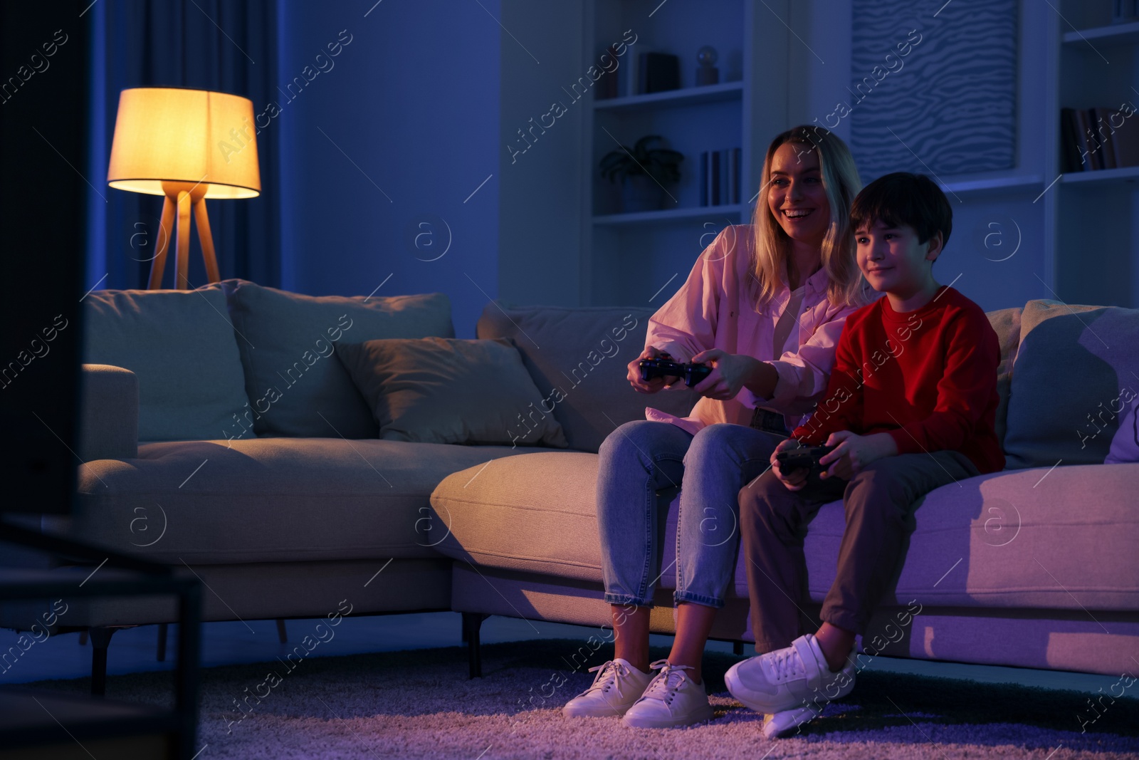 Photo of Happy mother and her son playing video games on sofa in living room