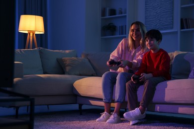 Happy mother and her son playing video games on sofa in living room