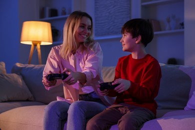 Photo of Happy mother and her son playing video games on sofa in living room