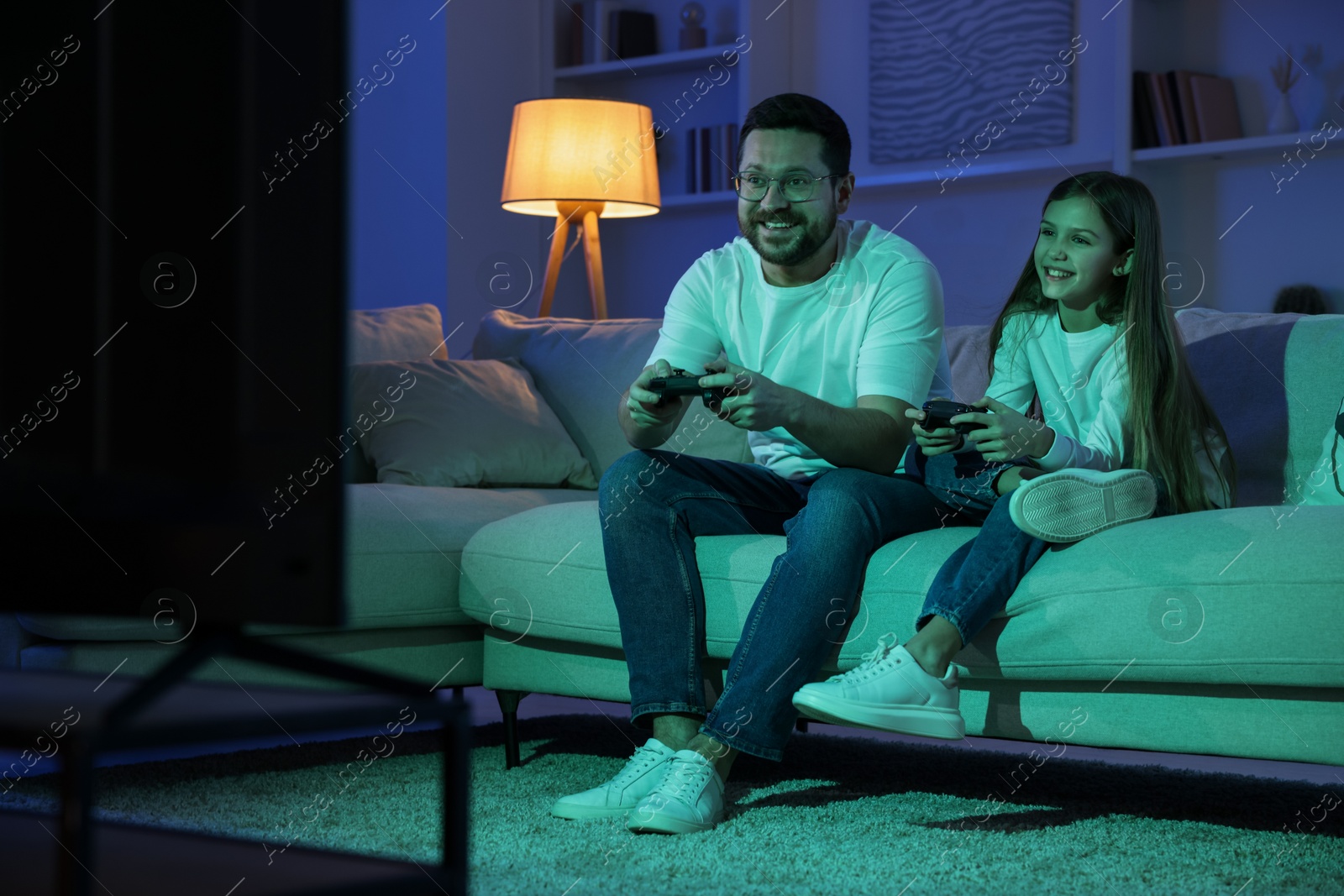 Photo of Happy father and his daughter playing video games on sofa in living room