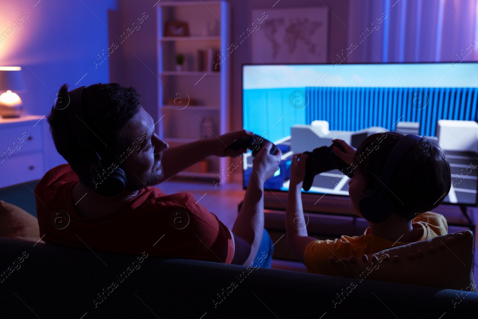 Photo of Father and his son playing video game on sofa in living room