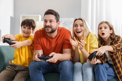 Photo of Happy family playing video games on sofa in living room