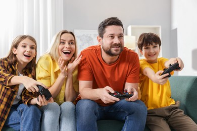 Photo of Happy family playing video games on sofa in living room