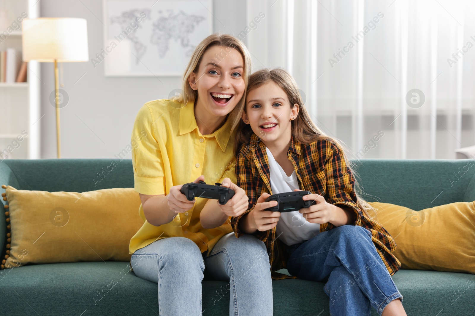 Photo of Happy mother and her daughter playing video games on sofa in living room