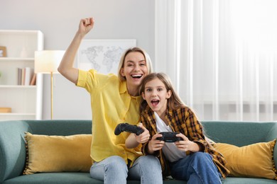 Photo of Happy mother and her daughter playing video games on sofa in living room