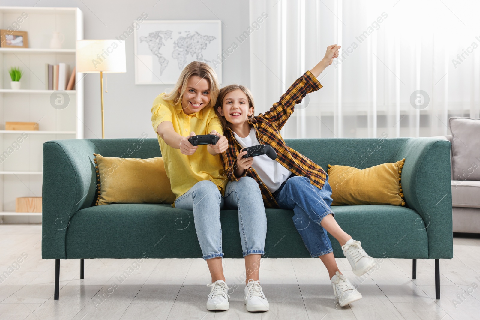 Photo of Happy mother and her daughter playing video games on sofa in living room