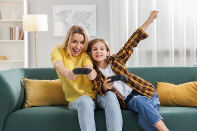 Photo of Happy mother and her daughter playing video games on sofa in living room