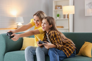 Photo of Happy mother and her daughter playing video games on sofa in living room