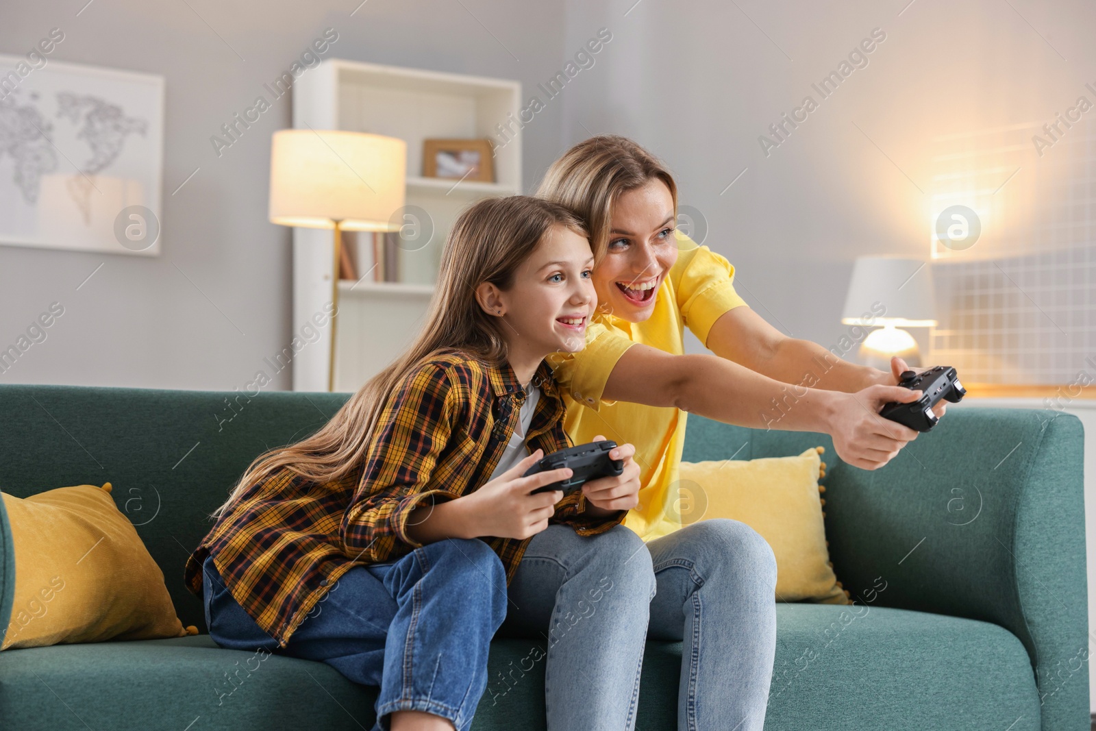 Photo of Happy mother and her daughter playing video games on sofa in living room