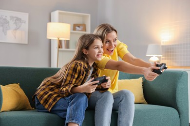 Photo of Happy mother and her daughter playing video games on sofa in living room