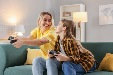 Photo of Happy mother and her daughter playing video games on sofa in living room