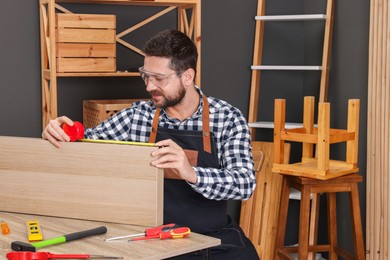 Photo of Relaxing hobby. Man measuring wooden plank with tape at table in workshop