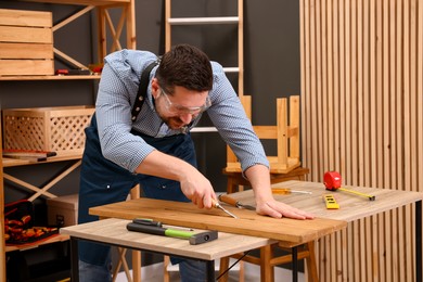 Photo of Relaxing hobby. Man working with wooden plank and chisel at table in workshop