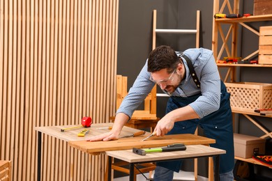 Photo of Relaxing hobby. Man working with wooden plank and chisel at table in workshop