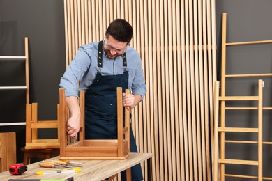 Photo of Relaxing hobby. Man assembling wooden chair with screwdriver at table in workshop, space for text