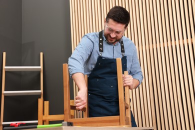 Photo of Relaxing hobby. Man assembling wooden chair with screwdriver at table in workshop, low angle view