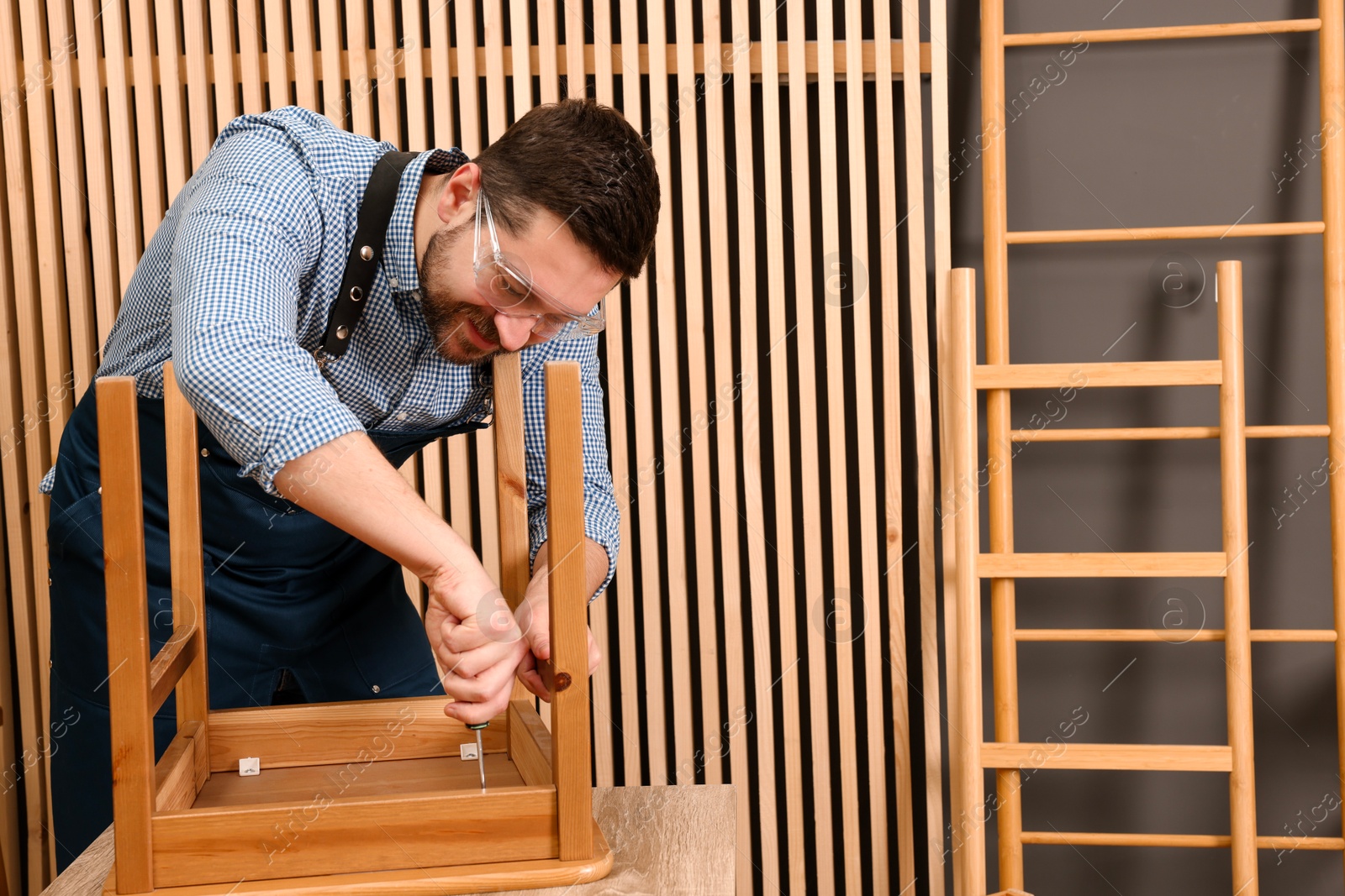 Photo of Relaxing hobby. Man assembling wooden chair with screwdriver at table in workshop, space for text