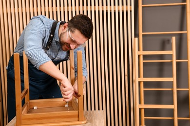 Photo of Relaxing hobby. Man assembling wooden chair with screwdriver at table in workshop, space for text