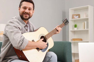 Photo of Relaxing hobby. Smiling man playing guitar on sofa at home