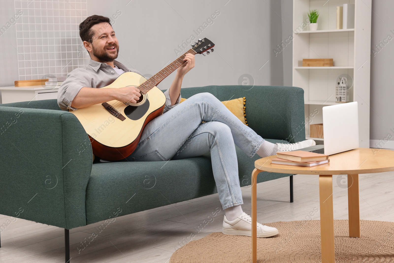 Photo of Relaxing hobby. Happy man playing guitar on sofa at home