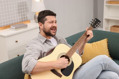 Photo of Relaxing hobby. Man playing guitar and singing on sofa at home