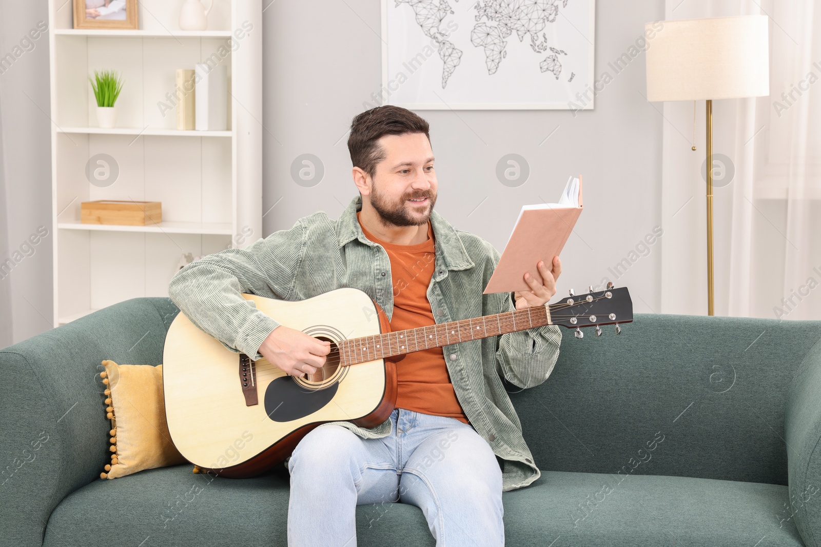 Photo of Relaxing hobby. Smiling man with guitar and book on sofa at home